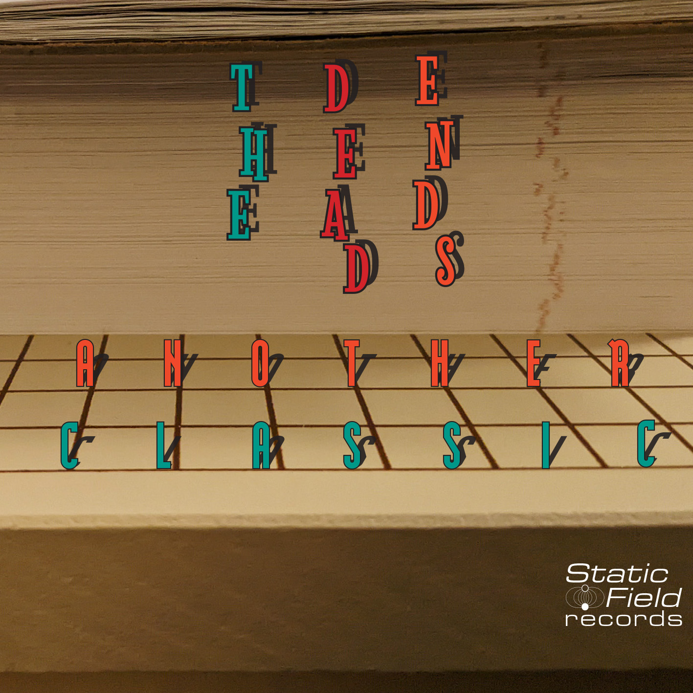 The cover features the band name 'The Dead Ends' stylized in all caps in front of a stack of cut, looseleaf notebook paper on an old wooden guillotine paper trimmer with red grid markings. The album title 'Another Classic' is set in a more modern, sans-serif font upon the board along the horizontal grid lines. Both titles are set in blue, red, and orange lettering and have shadowing from a light source on the left subjective to the photo. The record label logo for 'Static Field Records' includes a wordmark in the Stereowide font and an icon with a positive and negative diode with magnetic waves joining them together. Design, photo credit, wordmarks, and logo (c) Andrew J.Roback (2026).